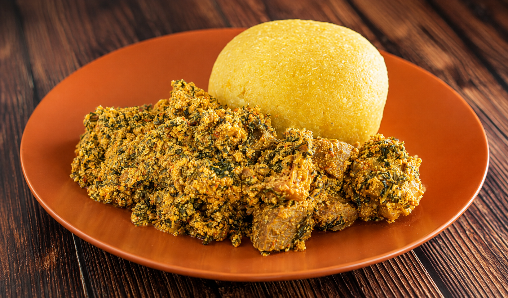 Egusi soup with meat served alongside a mound of yellow swallow on an earthen plate