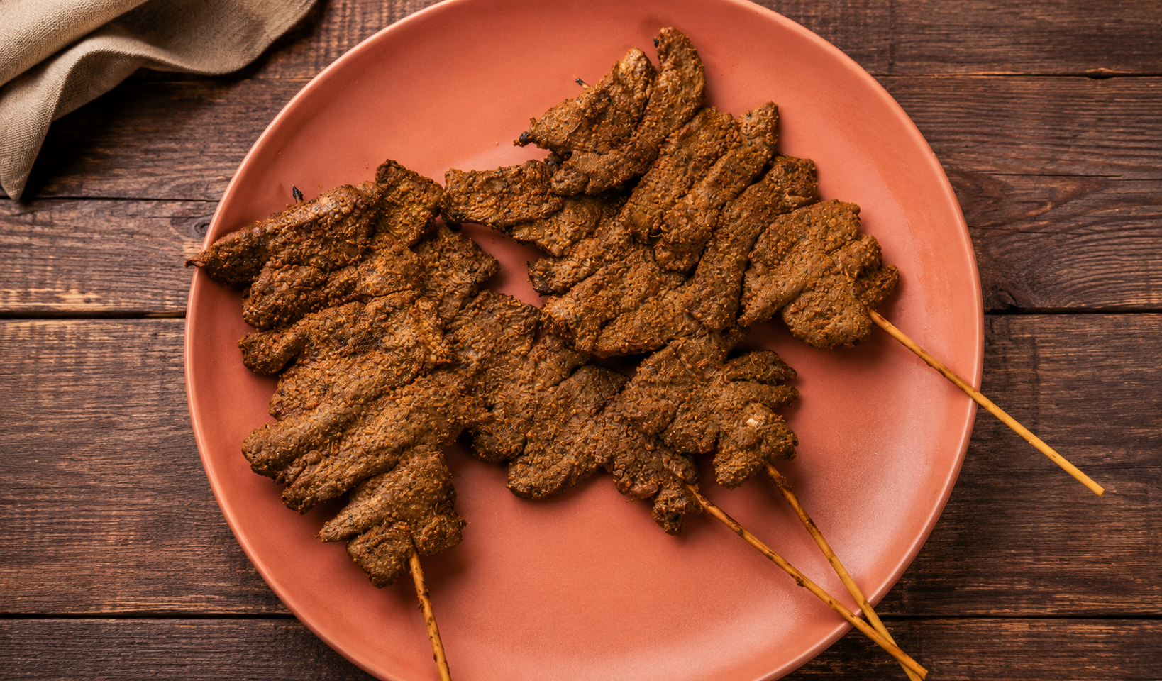 Thinly sliced yaji-spiced suya beef on skewers on a terracotta plate